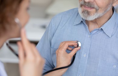 Close up young female general practitioner or cardiologist using stethoscope, checking heartbeat or listening lungs sounds of middle aged elder retired male patient at checkup appointment in hospital.